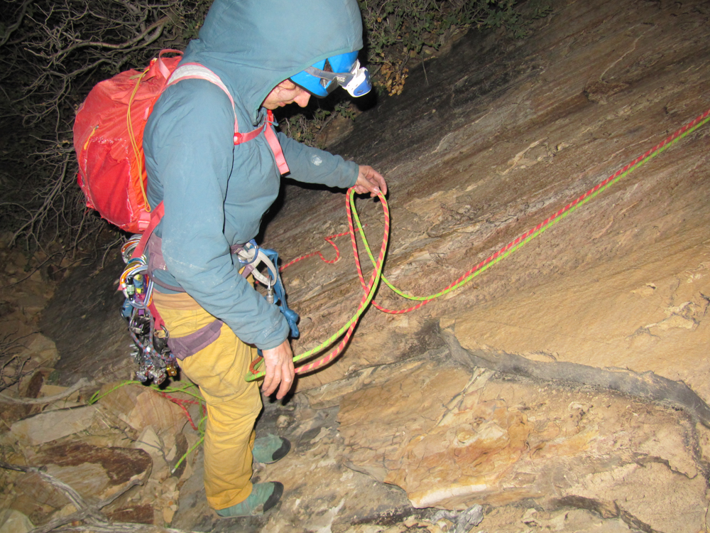 person with backpack on and two climbing ropes in hand. they are wearing a headlamp and it is dark.